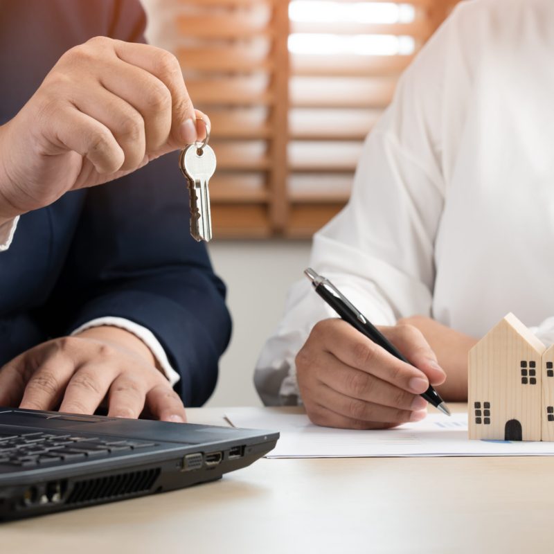 Businessman and woman to sell or buy house property as broker and client sign contract and payment before give house key to access building. Mortgage and other financial deal for home.